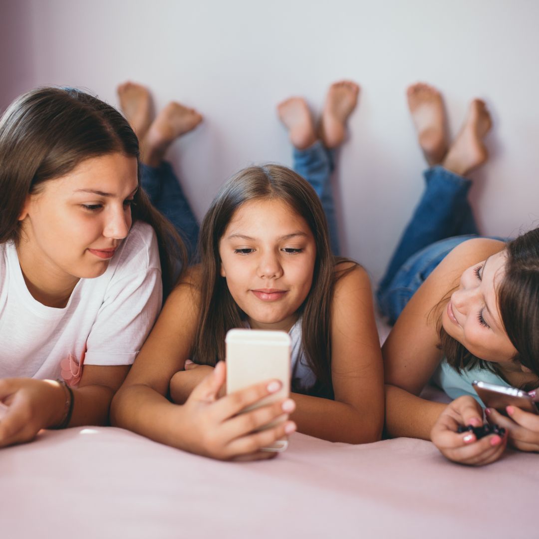 Flickorna ligger på golvet och tittar på sina mobiltelefoner.