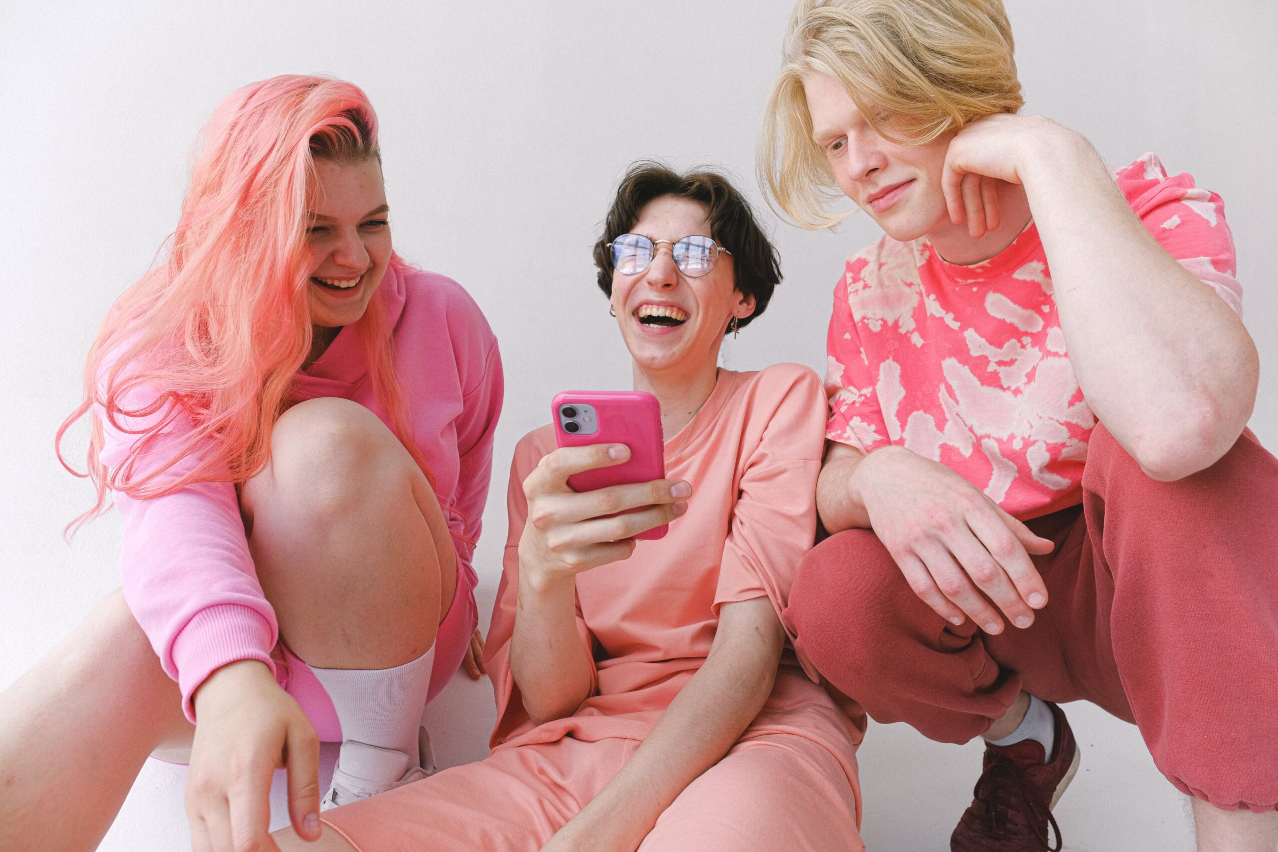 Kolme nuorta nauravat yhdessä ja katsovat älypuhelinta